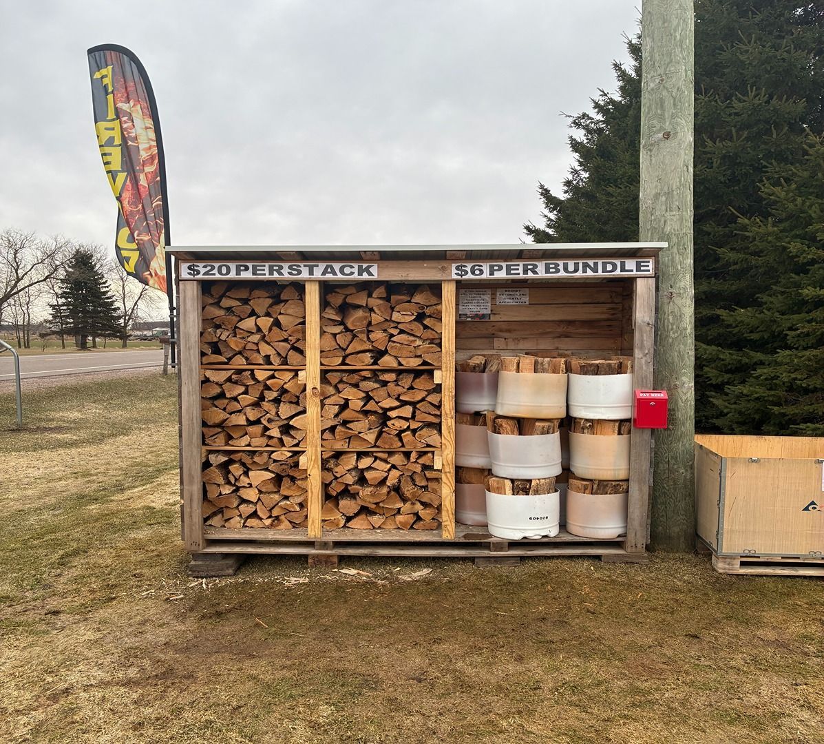 Roadside self-serve stand with stacked firewood and buckets under a cloudy sky