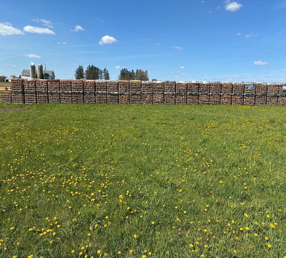 Wide green field with yellow flowers in front of a long hay bale wall under a blue sky