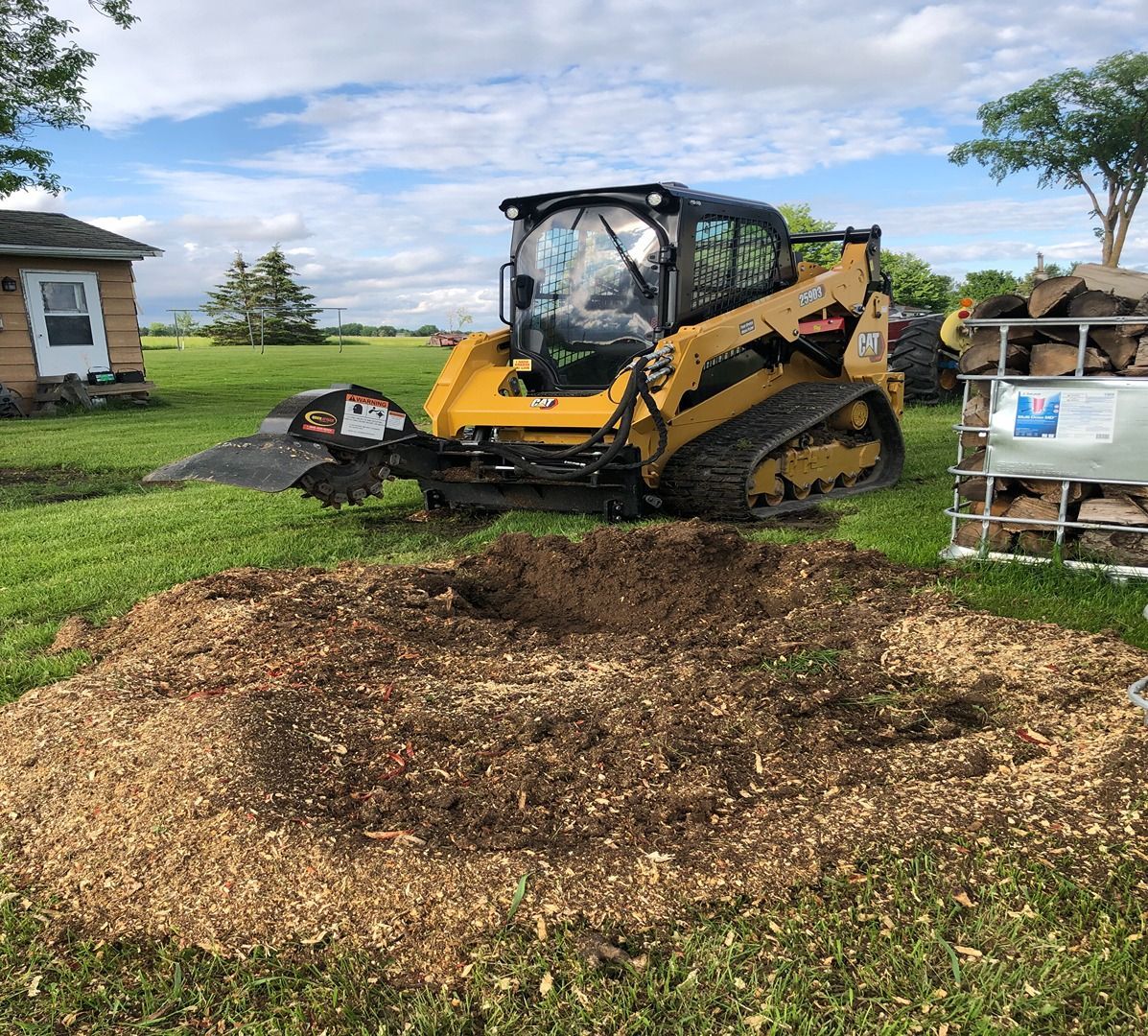 Yellow skid-steer loader next to a large mulch pile on a grassy field under a cloudy sky