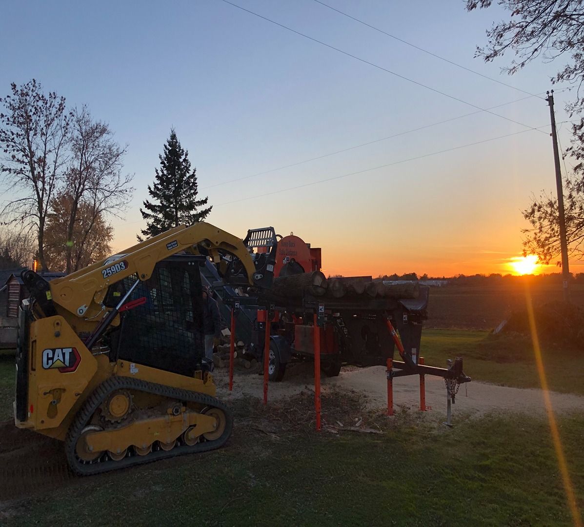 Yellow CAT tractor at sunset beside farm equipment in a field with trees and power lines.