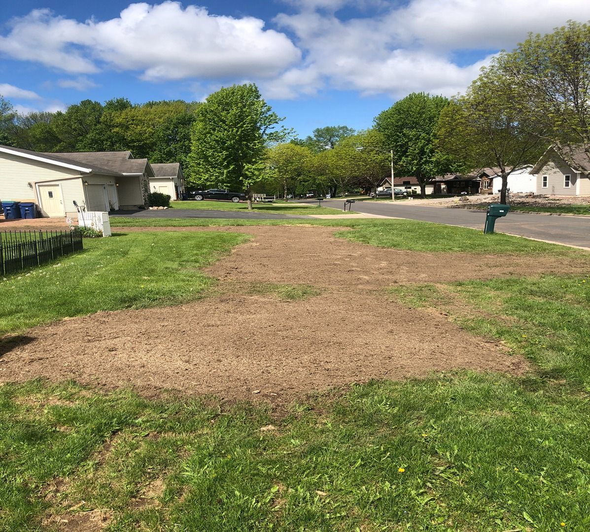 Suburban street with a large brown patch in a green lawn under a partly cloudy sky