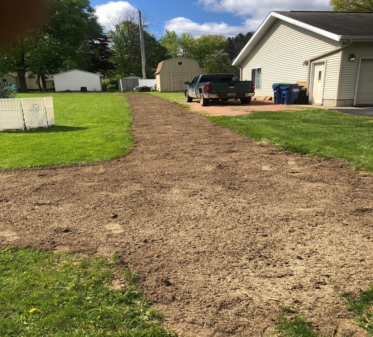 Gravel driveway leading to a beige house with a black pickup truck parked beside it.
