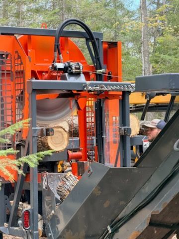 Orange logging machine processing a tree trunk beside a worker in a forest
