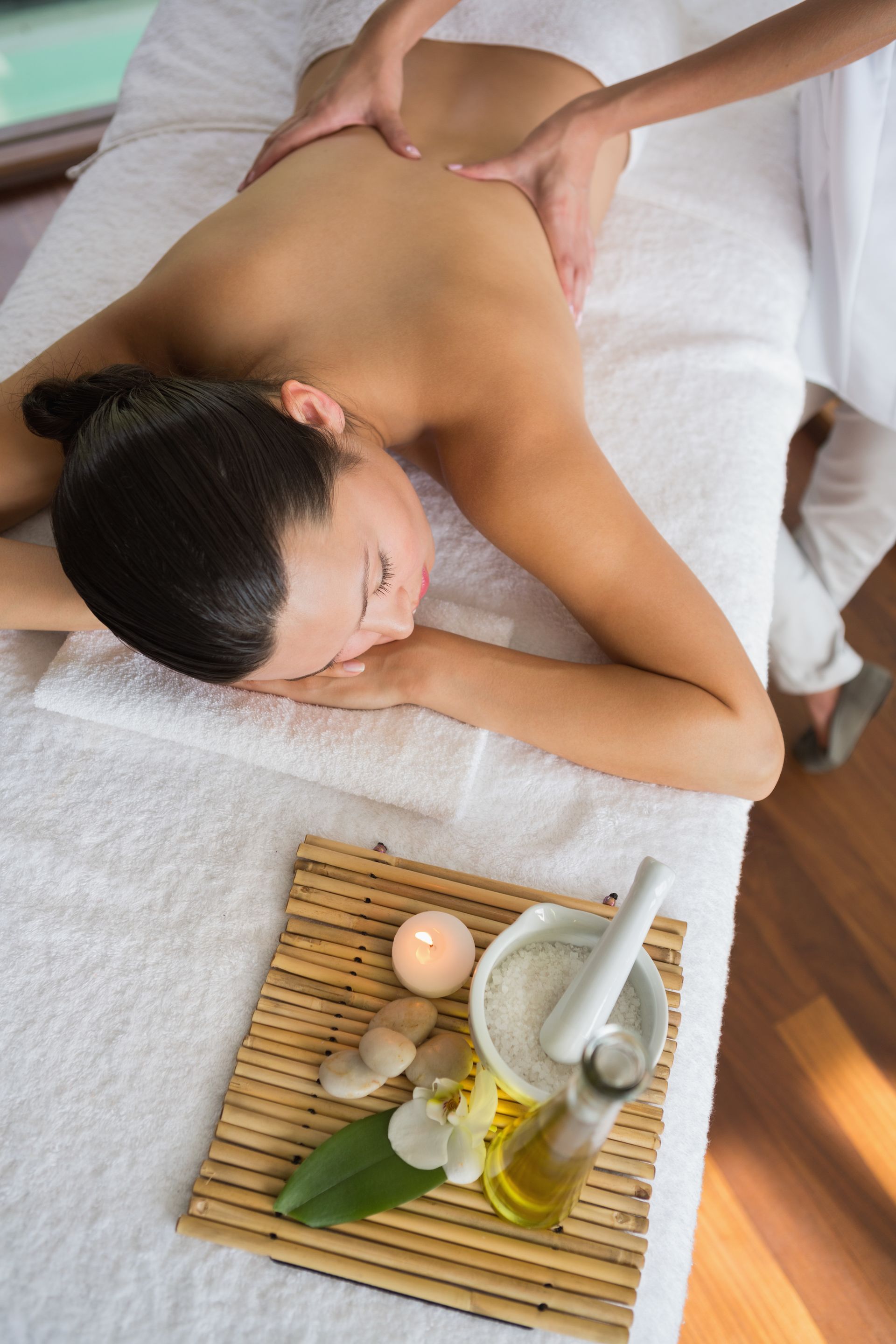 Mujer recibiendo un masaje de espalda en un spa. Aceite y vela sobre una esterilla de bambú.