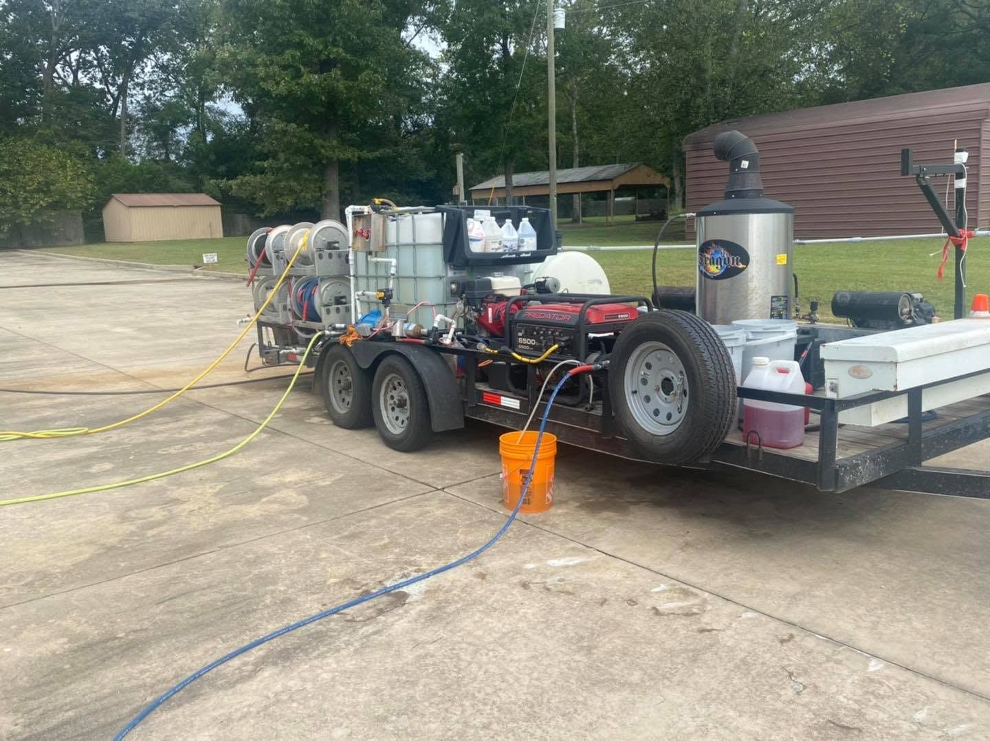 Trailer-mounted pressure washing setup with tanks, hoses, and equipment in a concrete yard
