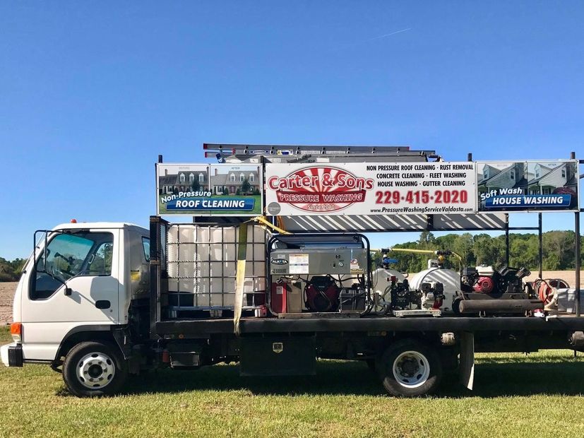 Flatbed truck with billboard-style signs parked on a road under a clear blue sky.