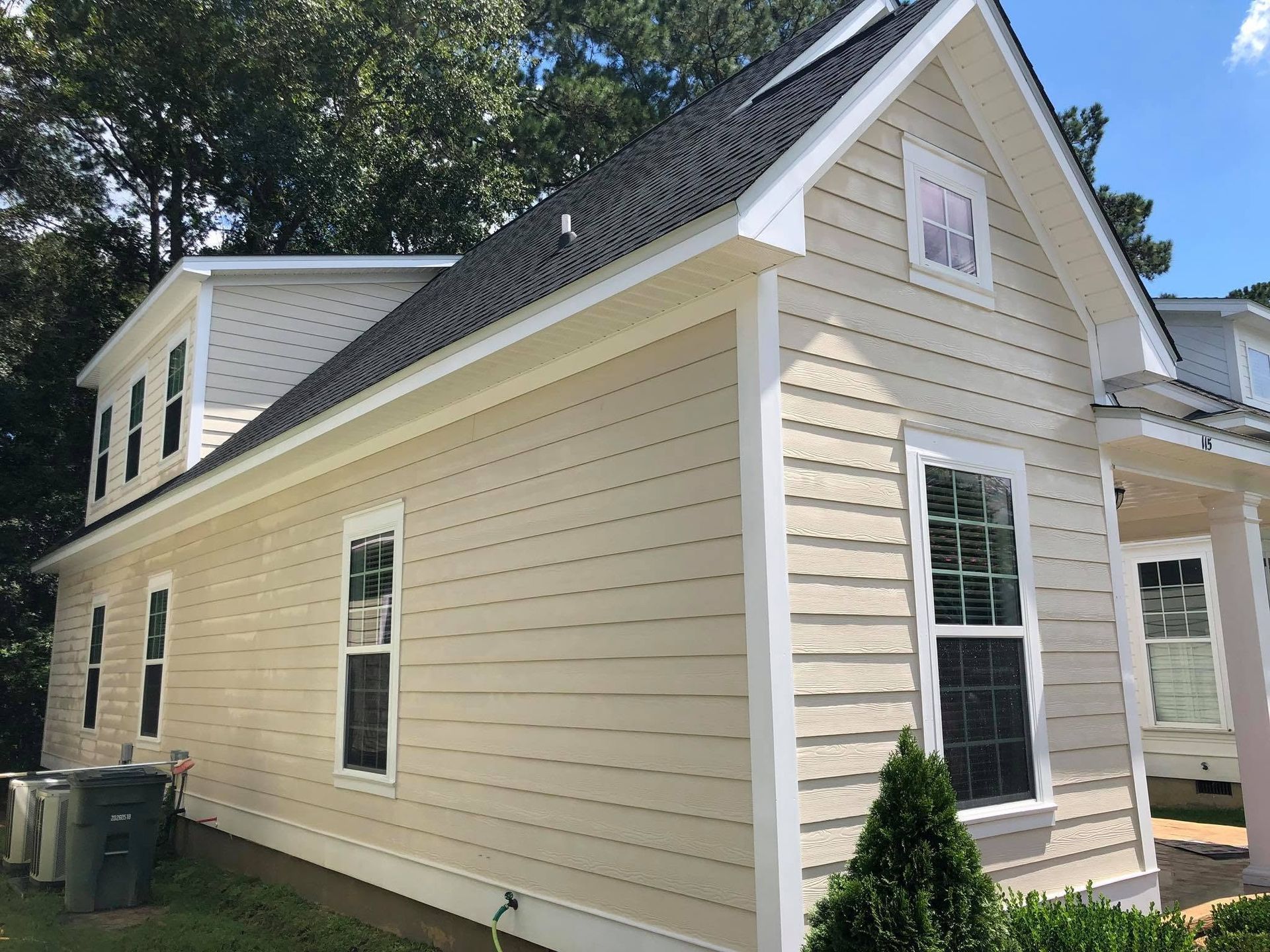 Side view of a beige house with white trim, black roof, and a small front entry porch.