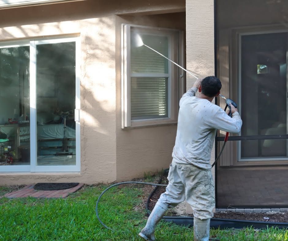 Person pressure-washing a house exterior beside windows and a sliding glass door