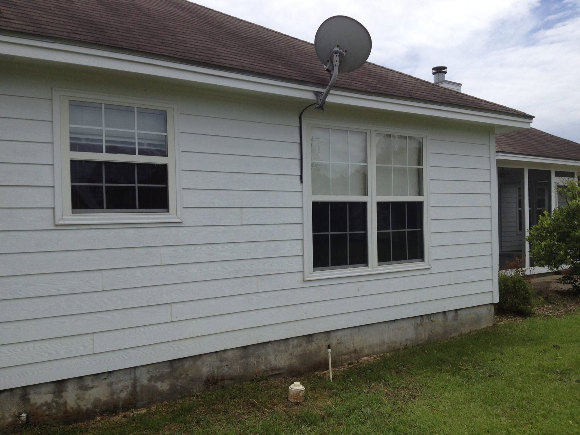 White house exterior with vinyl siding, two windows, and a satellite dish on the roof