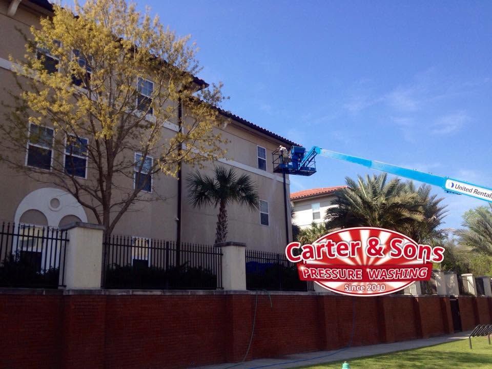 Carrell & Sons sign on a beige building behind a red brick wall and trees under a blue sky