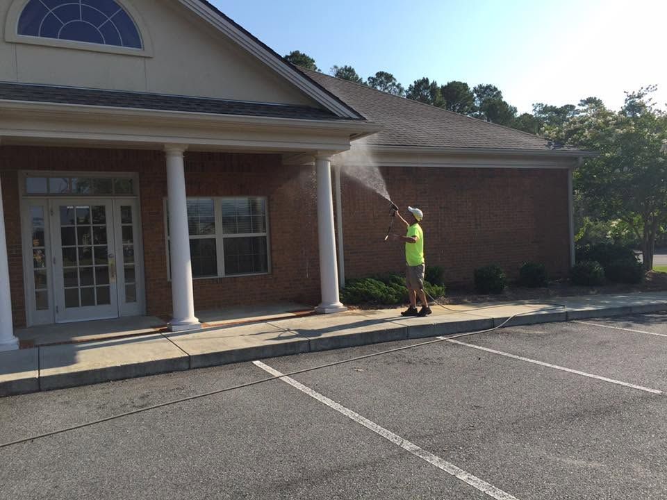 Worker spraying water on brick building entrance near empty parking lot