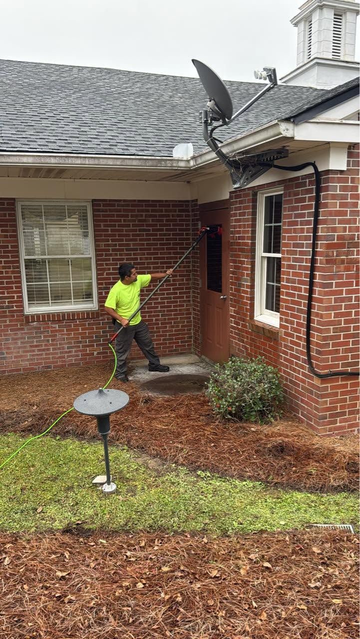 Worker in neon shirt clearing debris beside a brick house and roof gutter.