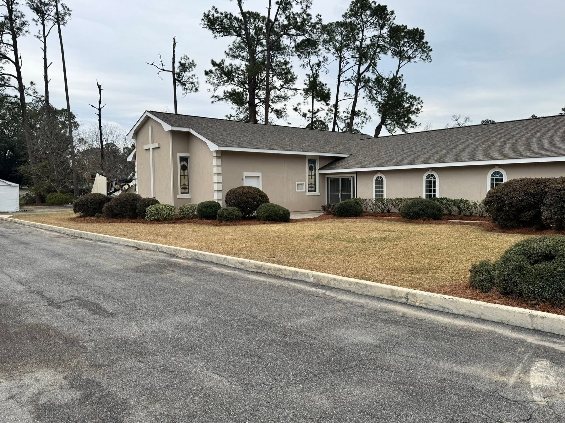 Single-story beige building with arched windows along a paved road on a cloudy day