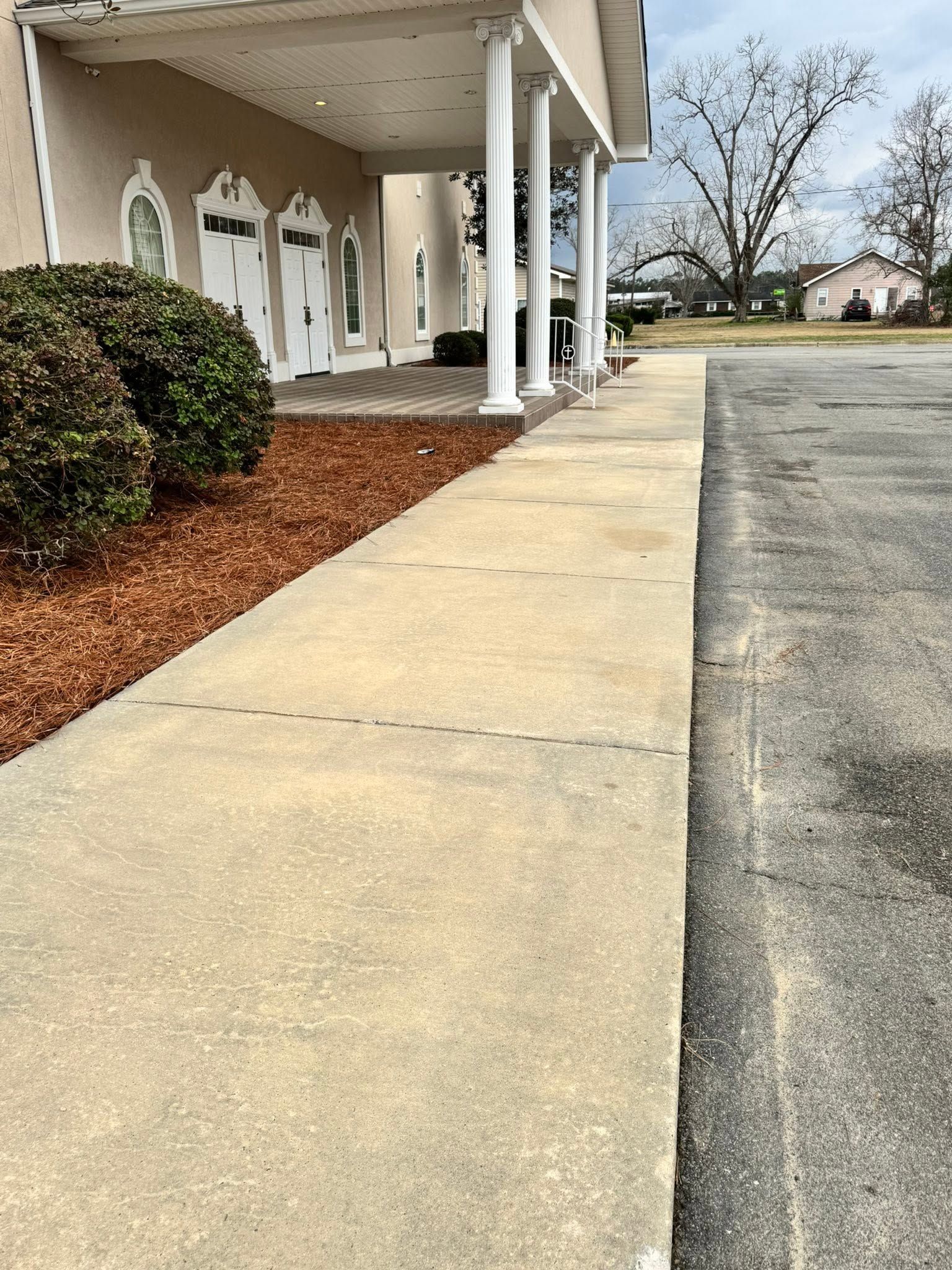 Sidewalk beside a beige building with white columns and an empty parking lot