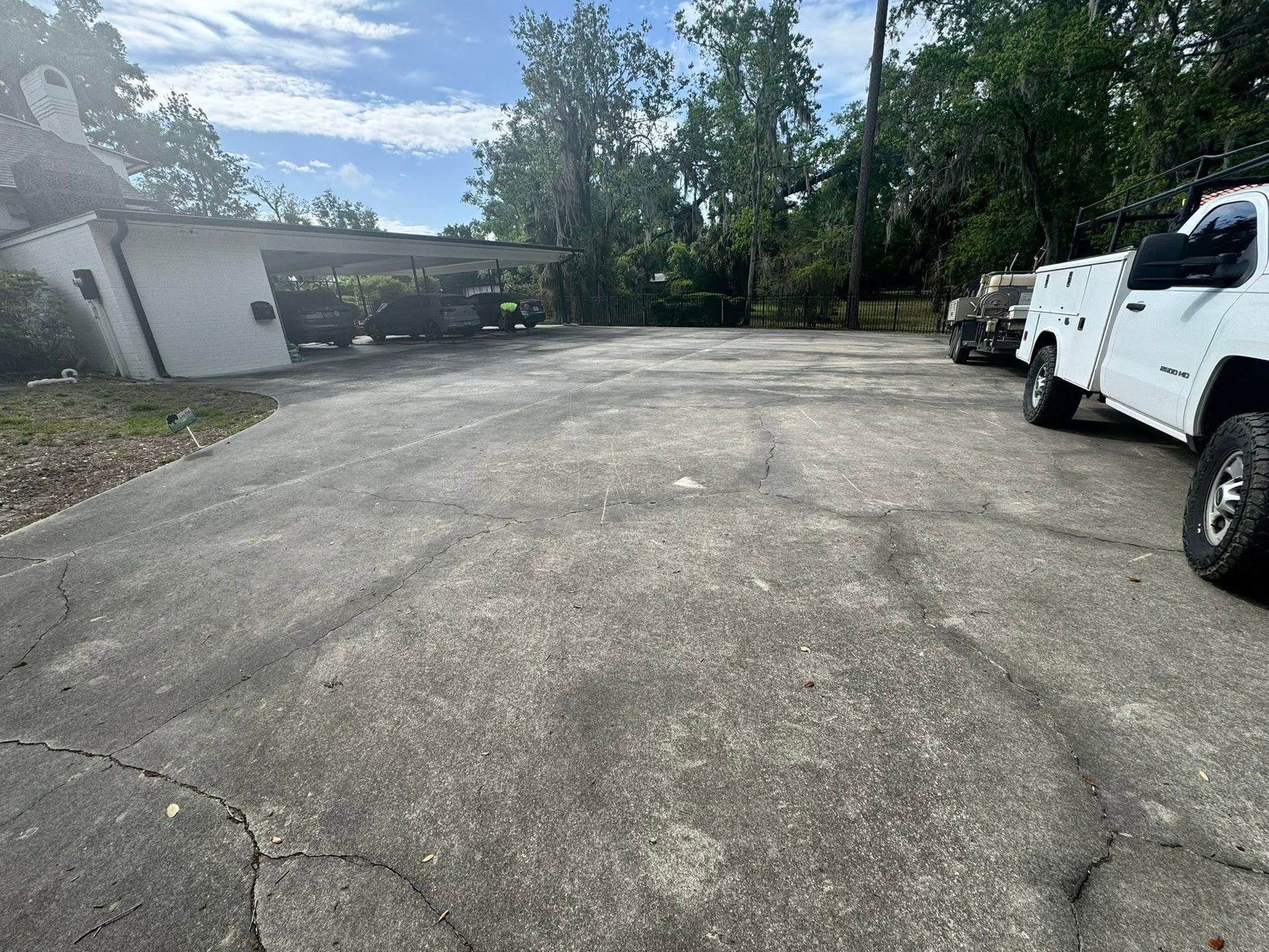 Wide cracked asphalt parking lot beside buildings and trees, with a white truck on the right.
