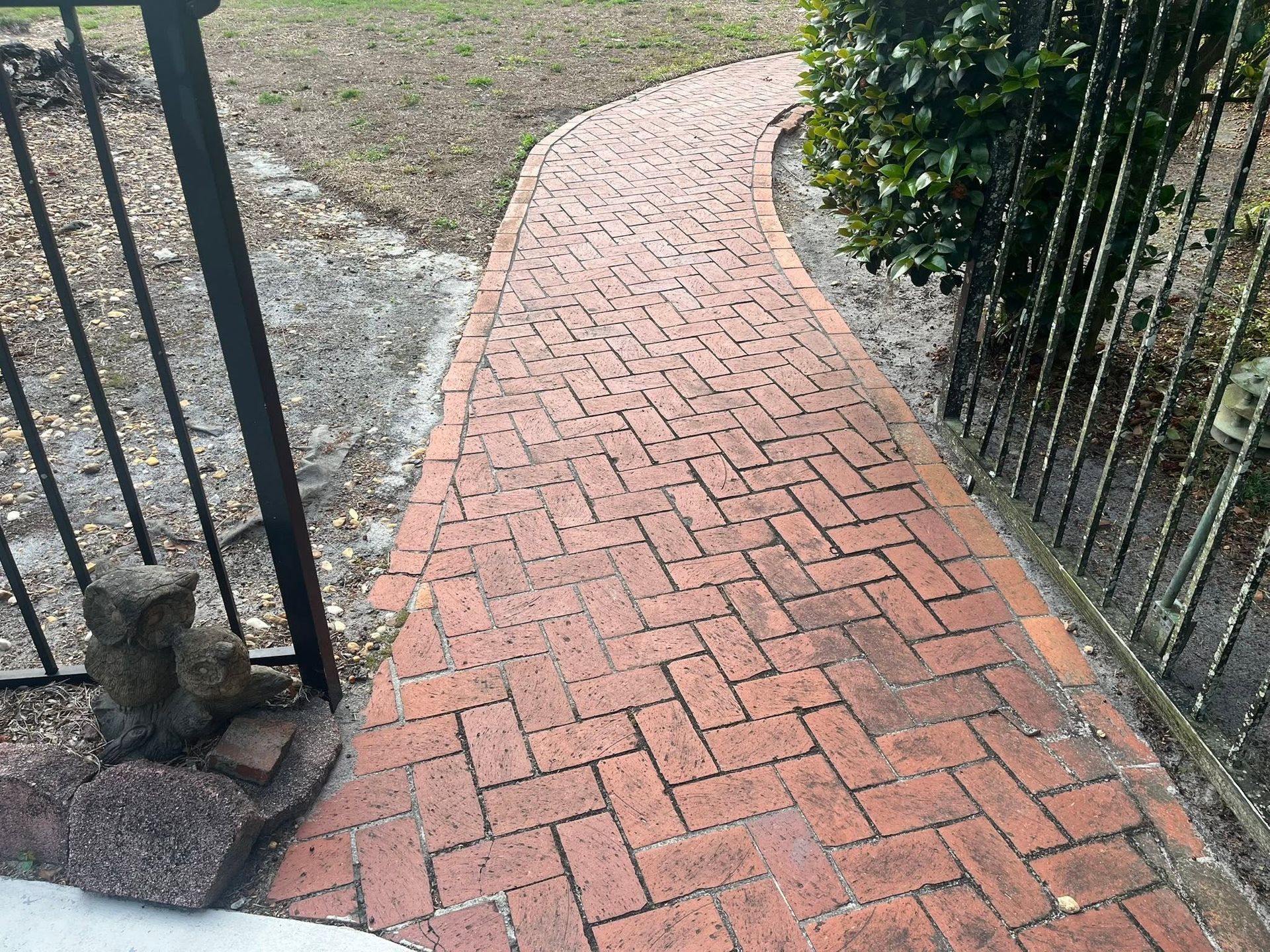 Brick walkway between black iron fences curving through a grassy yard