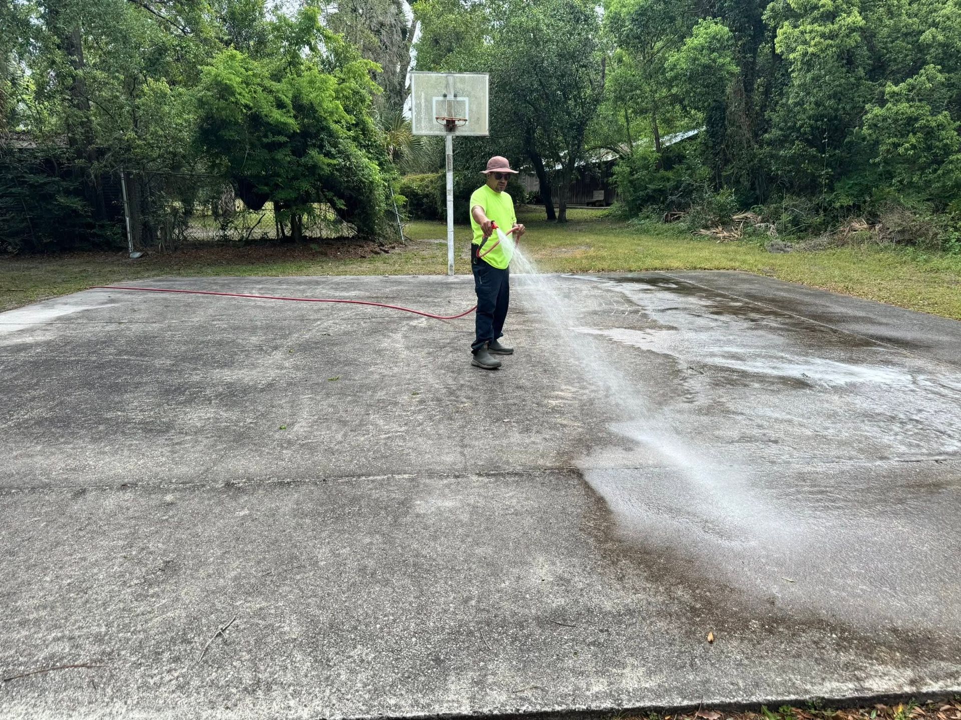 Person in a neon shirt standing on a wet outdoor basketball court near a hoop.
