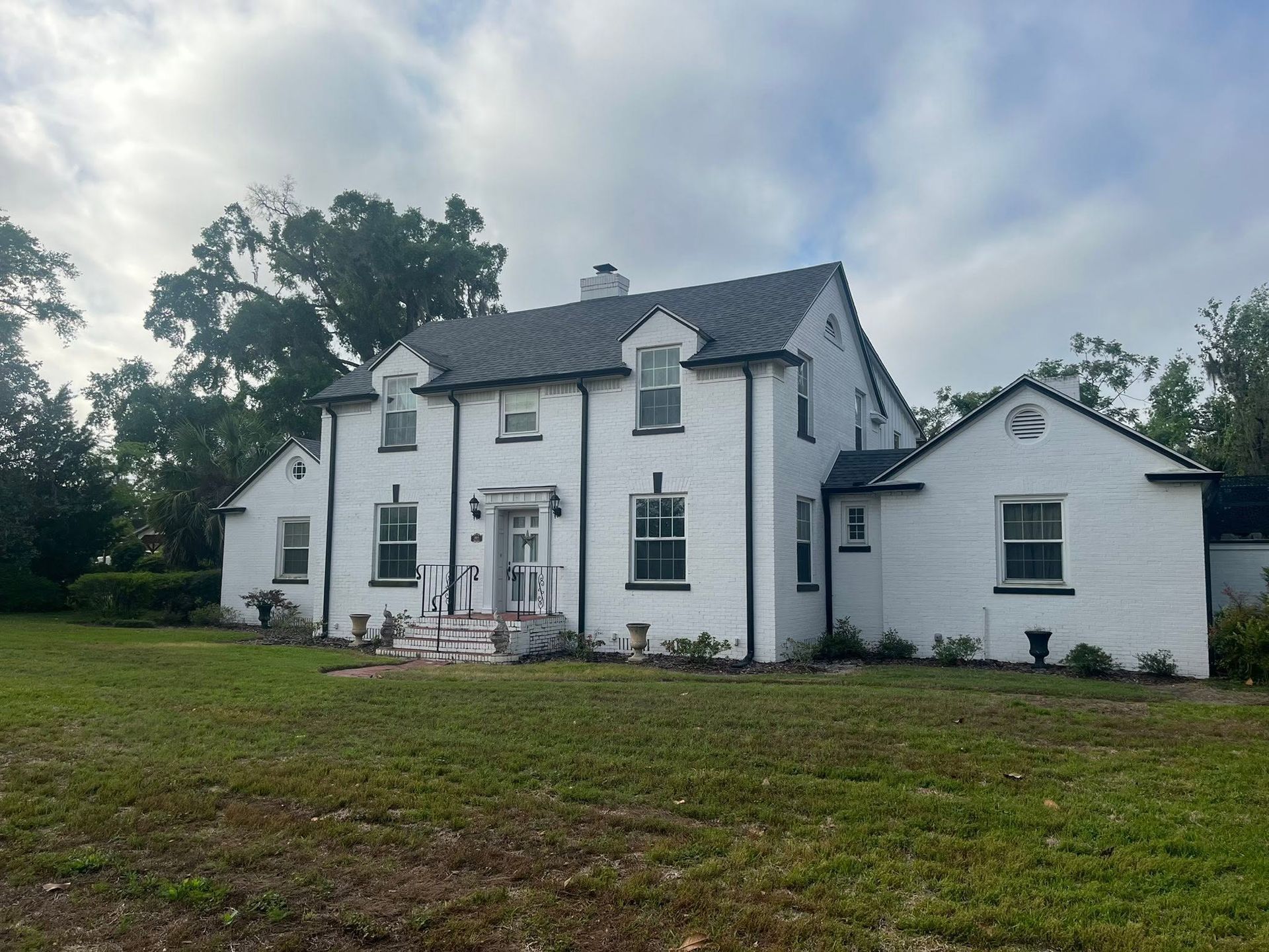 White two-story house with dark roof and large lawn under a cloudy sky