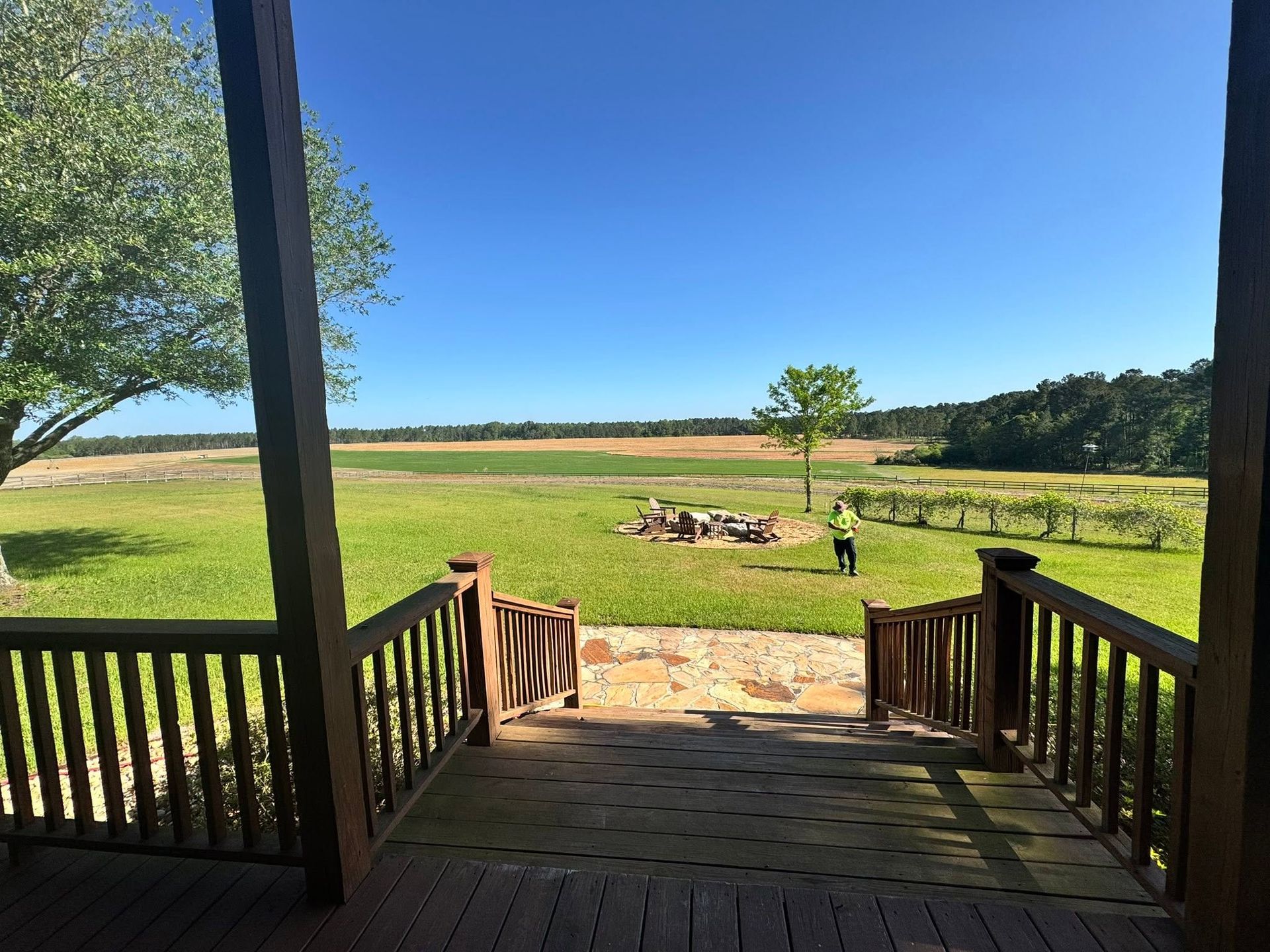 Porch overlooking a sunny grassy field with a small tree and a person in the distance