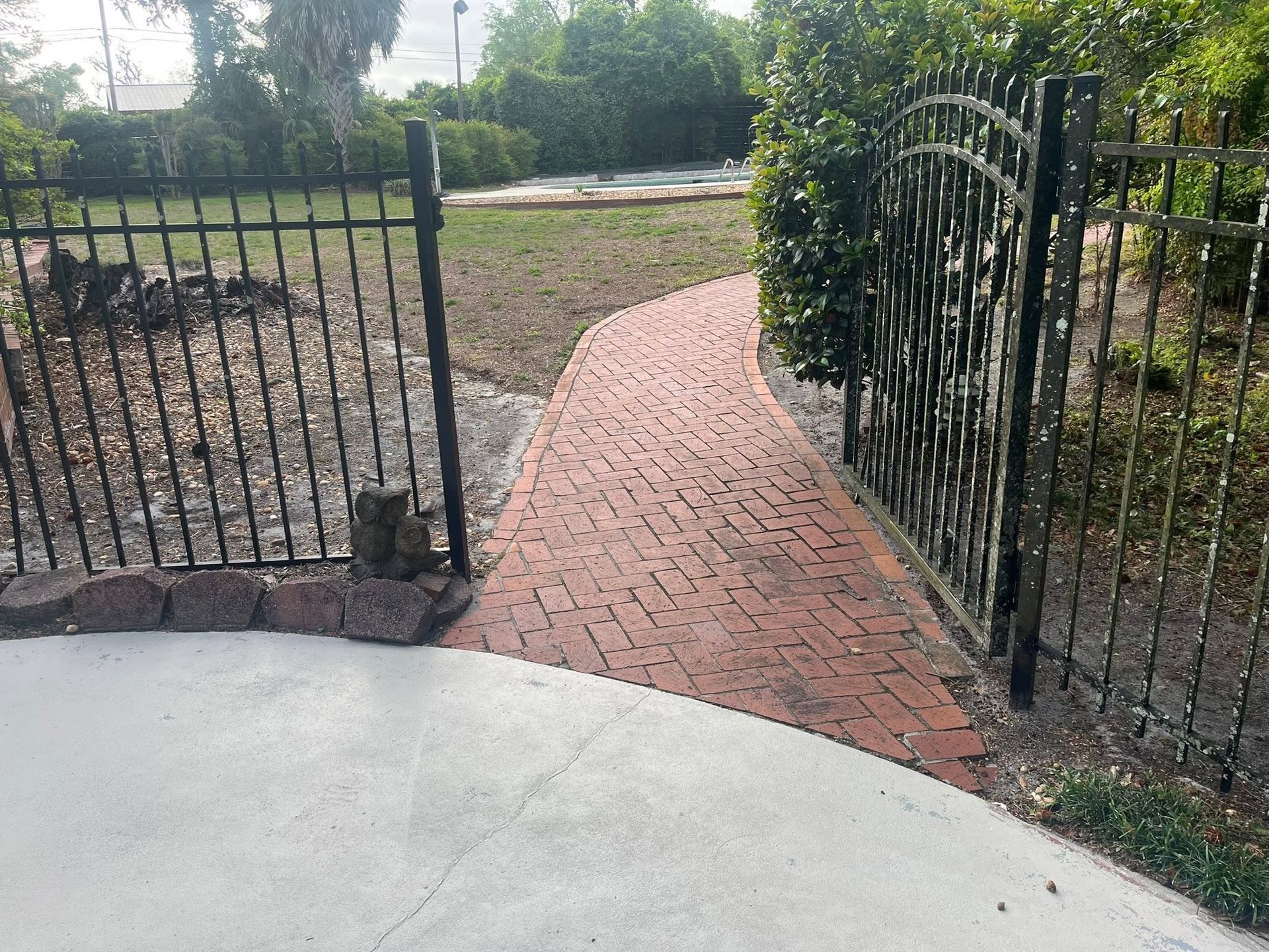 Brick garden path through open black metal gates leading to a yard.