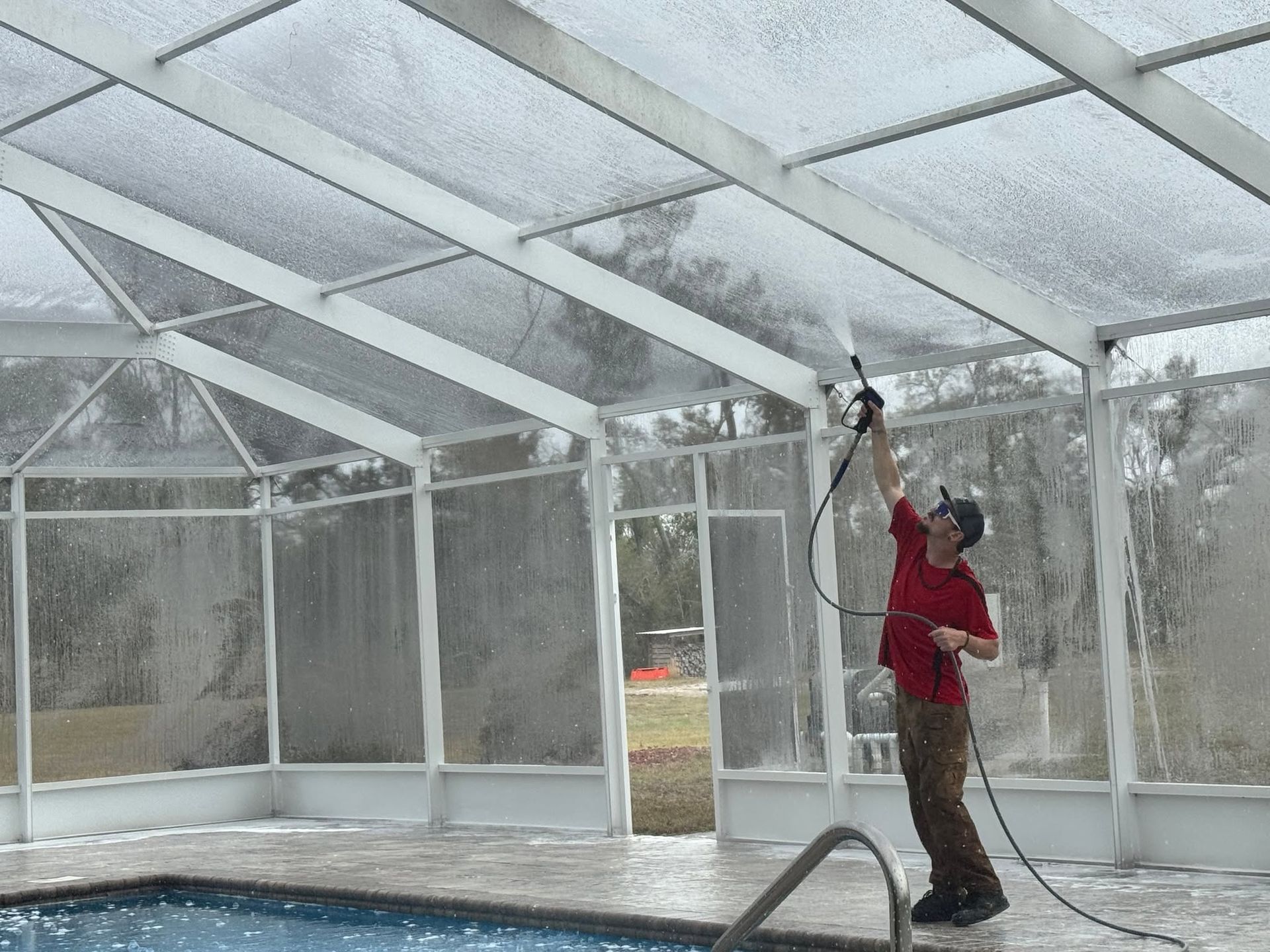 Person in red jacket spraying water inside a screened-in greenhouse structure.