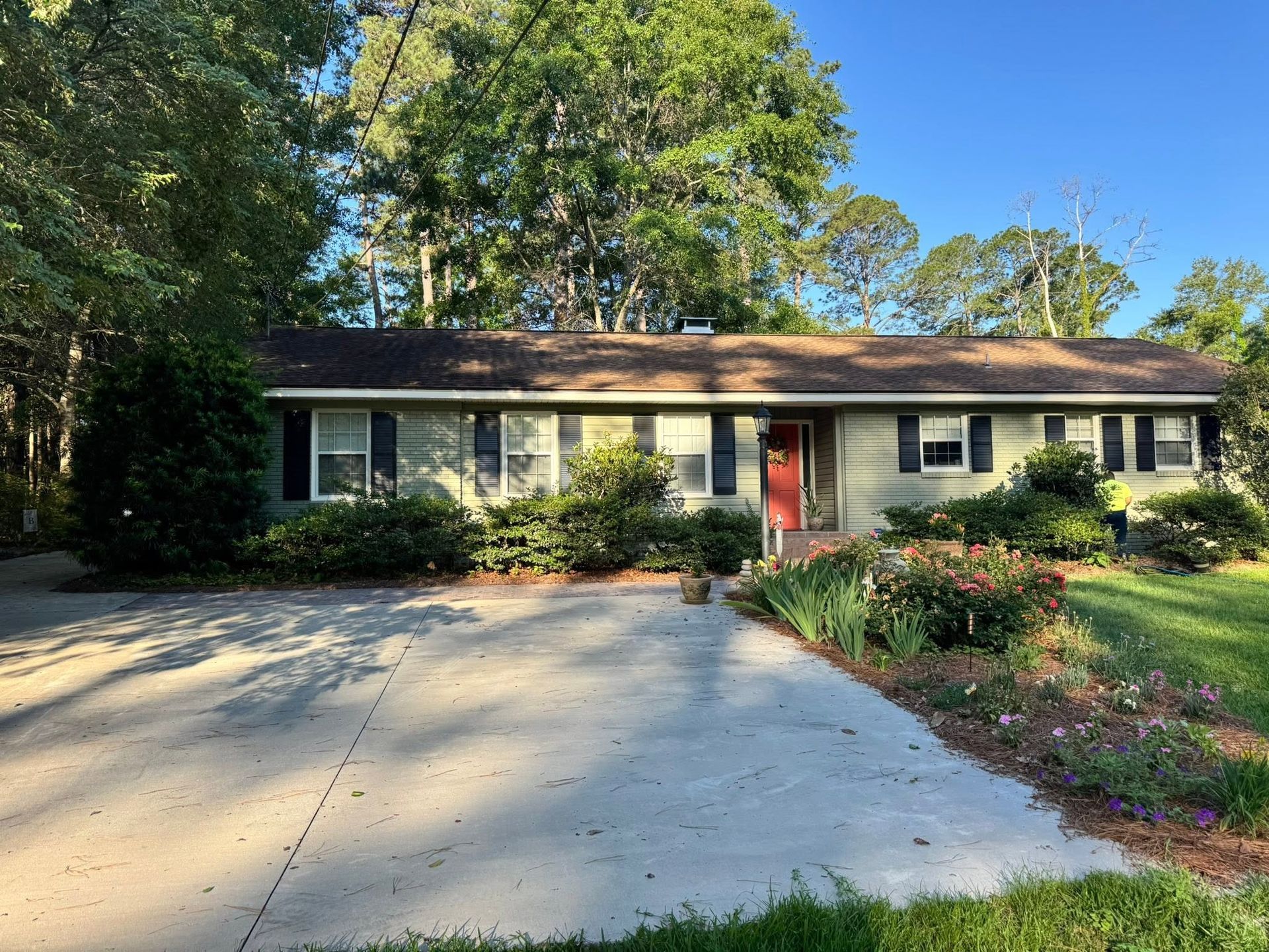 Single-story house with a driveway, red front door, and trees in the yard