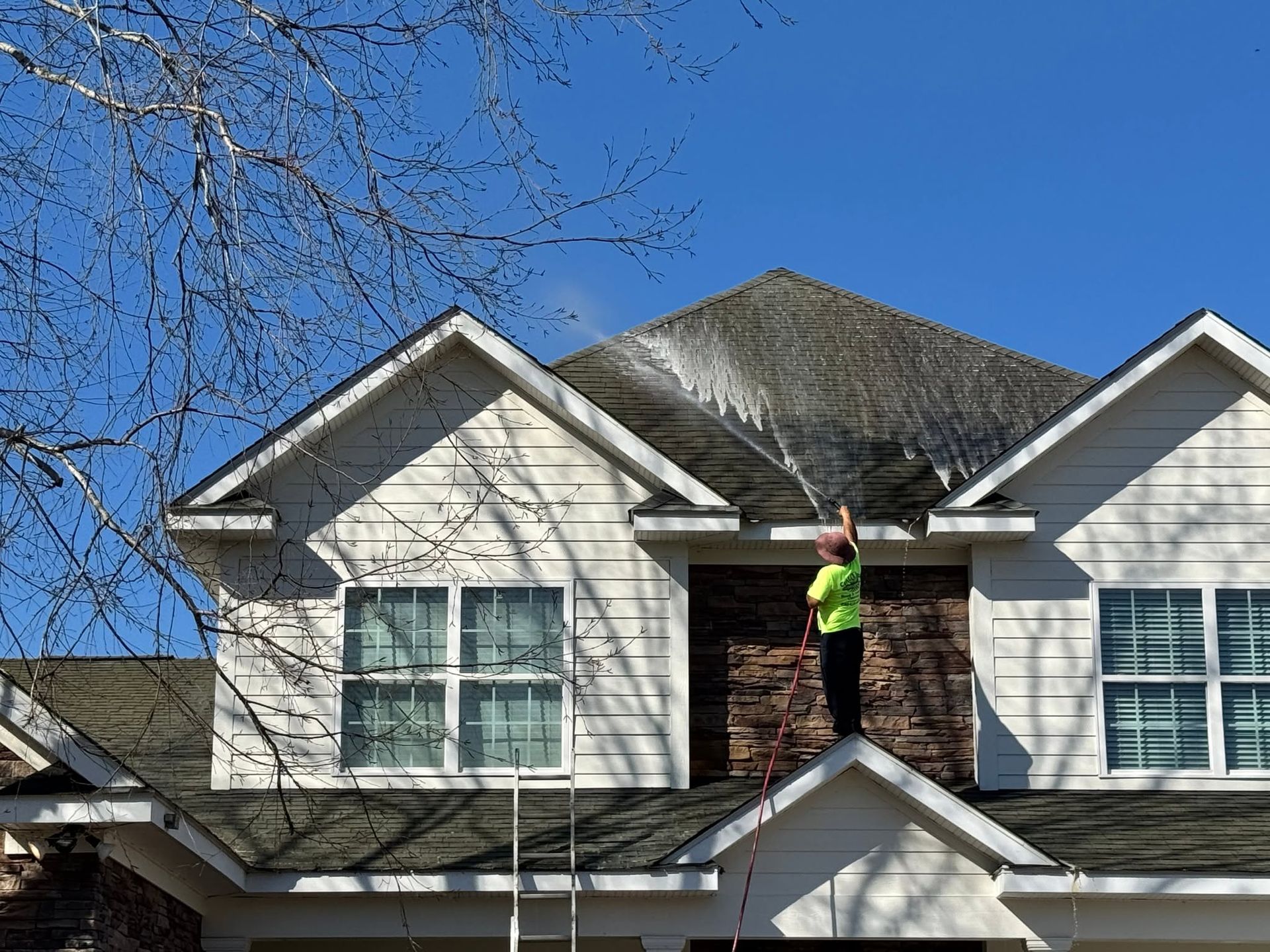 Worker on a roof repairing shingles on a white suburban house under a blue sky