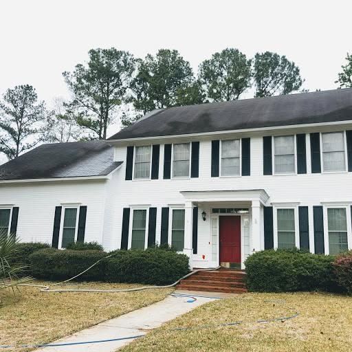 White two-story house with black shutters, red door, and a curved walkway in front