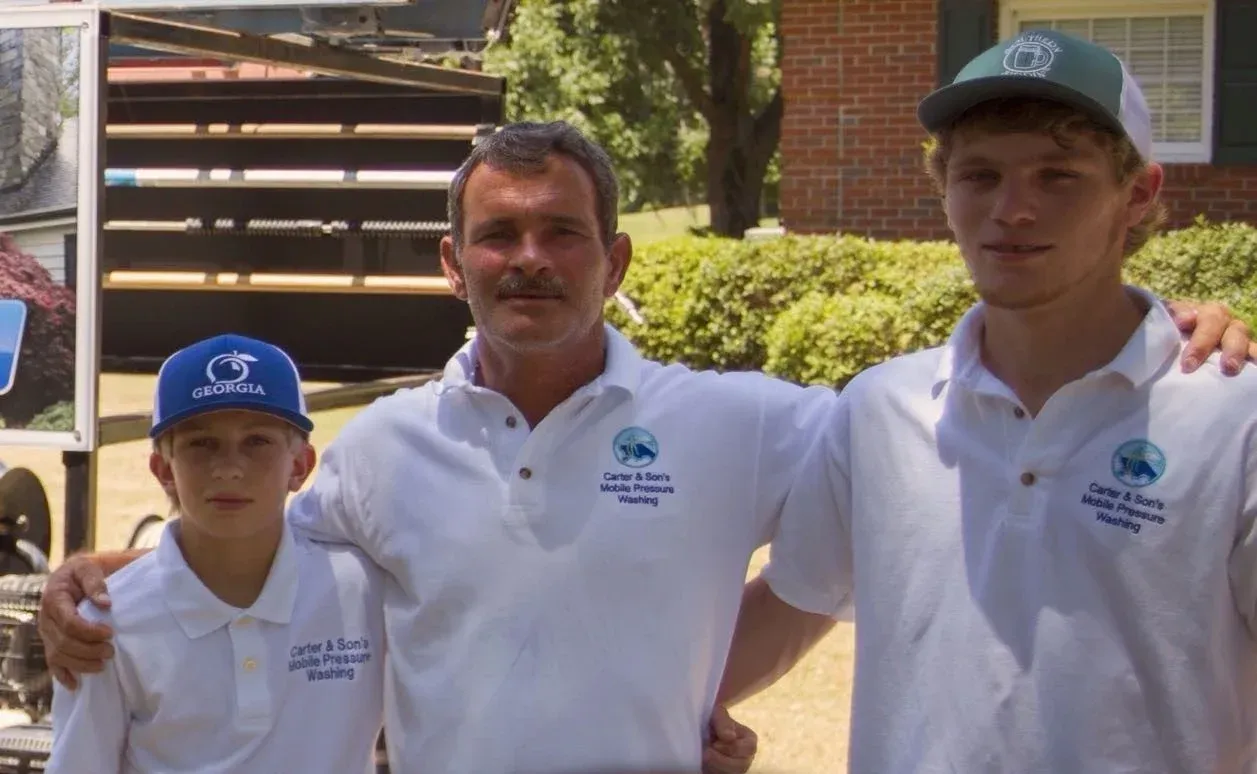 Three people in white polo shirts and caps standing outdoors in front of a brick building.