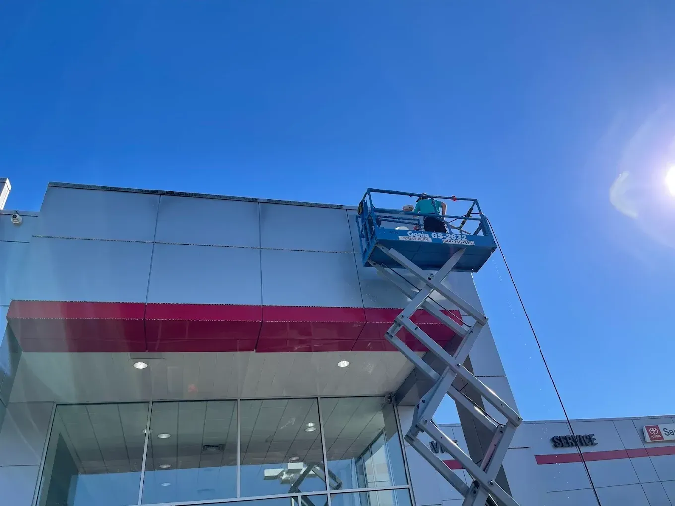Worker in a blue lift inspecting a building facade under a clear sky