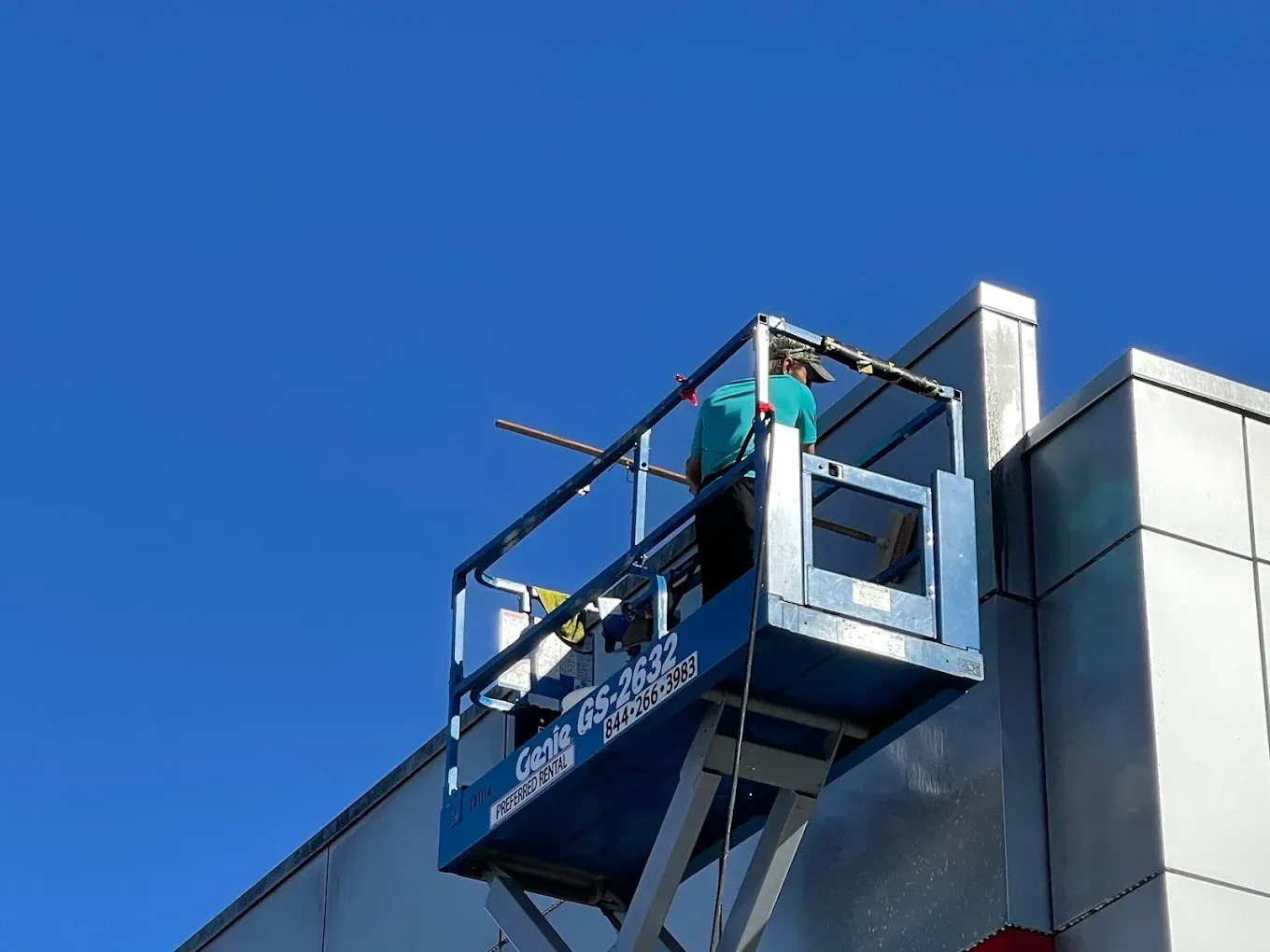 Worker in a blue lift inspecting the side of a building against a clear blue sky