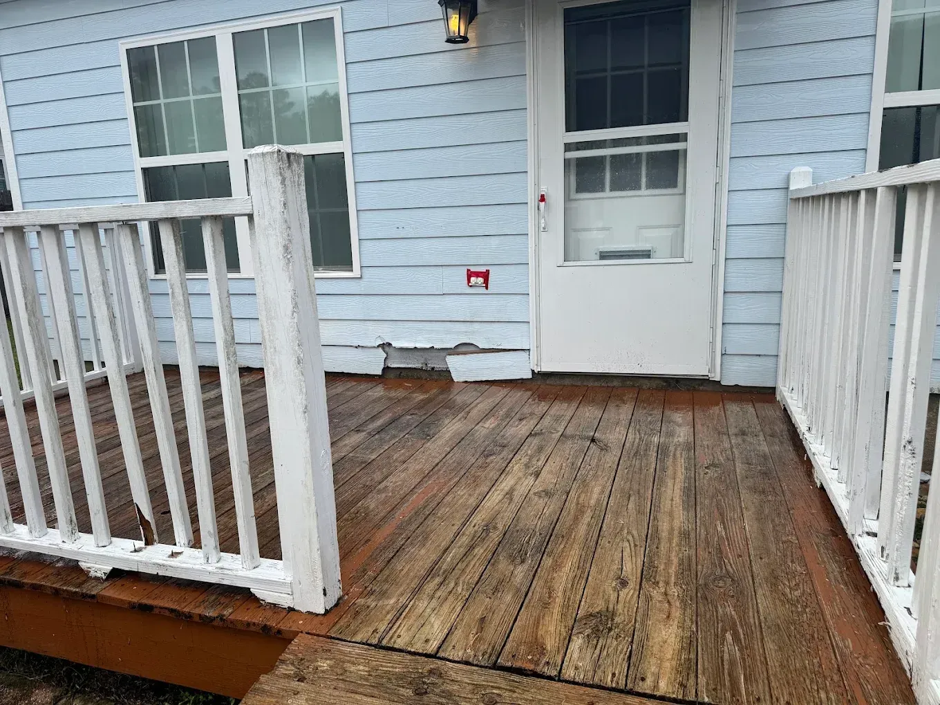 Weathered wooden porch with white railings, pale blue siding, and a white door.