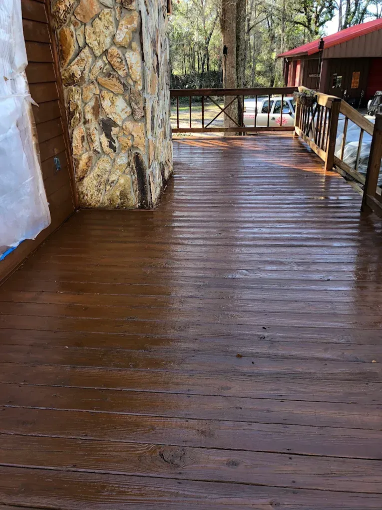 Wooden porch walkway beside a stone wall and railing, leading to an outdoor area