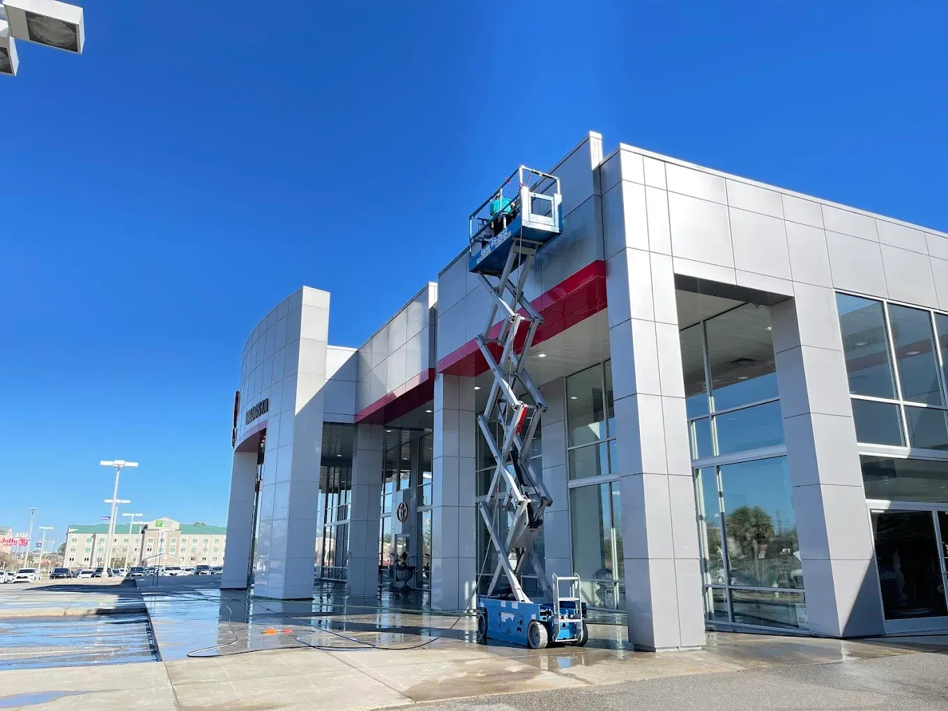Worker in a blue lift cleaning the exterior of a modern glass building on a sunny day
