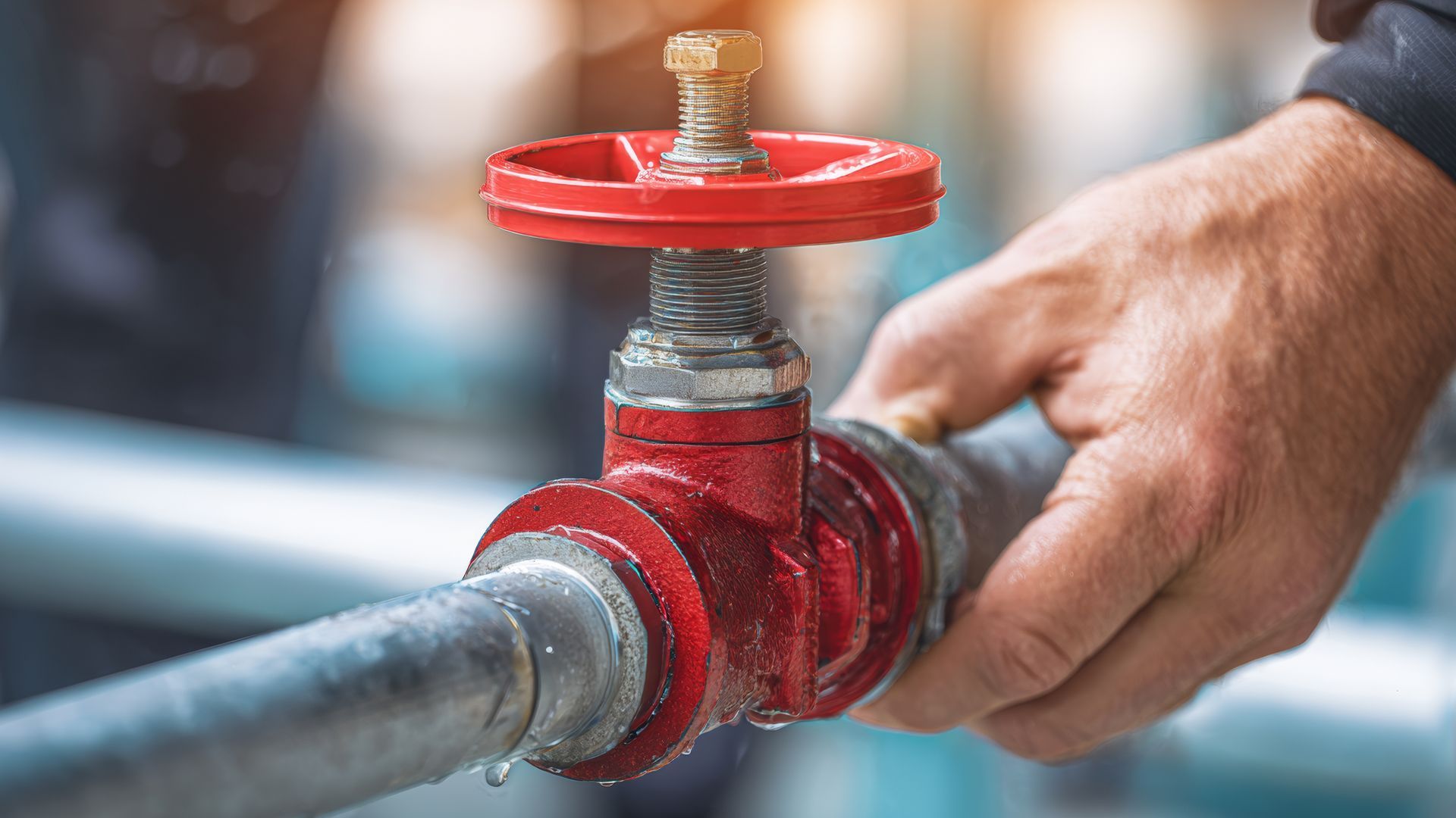 Photograph of a hand turning a red valve attached to a metal pipe. Photograph of a hand turning a red valve attached to a metal pipe.