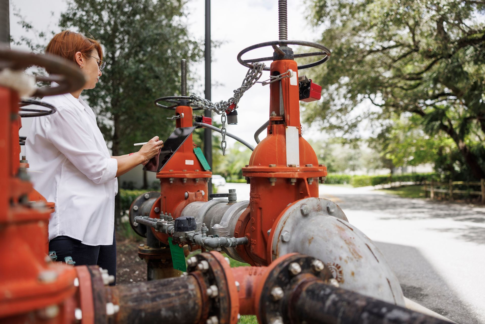Technician in white shirt, performing backflow device testing on red outdoor water system valves. Technician in white shirt, performing backflow device testing on red outdoor water system valves.