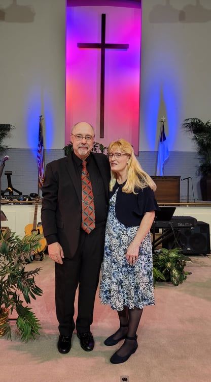 A man and a woman are standing in front of a cross in a church.