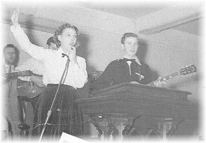 A man is playing a guitar and a woman is singing into a microphone.