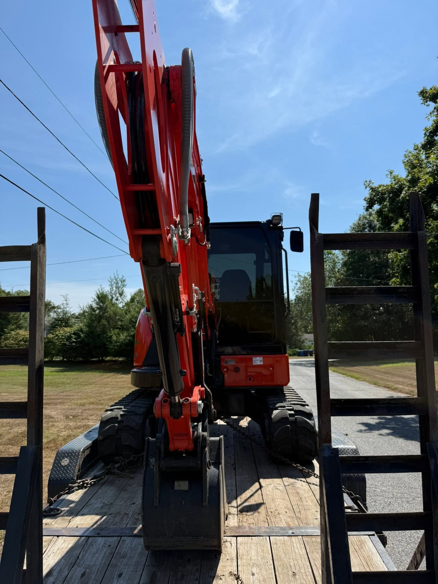 Red excavator on a flatbed trailer between open trailer ramps under a blue sky