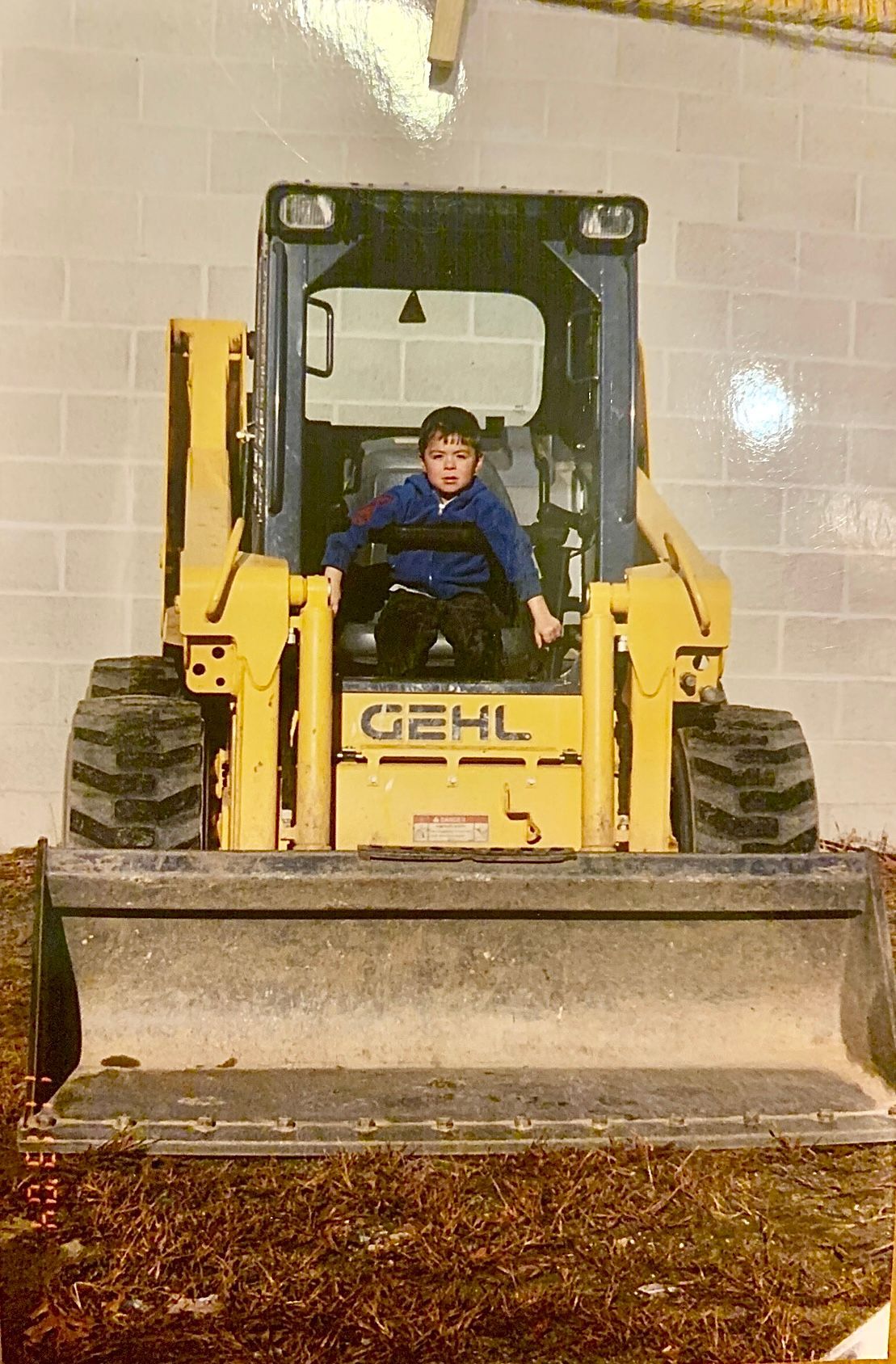 Child sitting in a yellow front loader inside a tiled indoor space