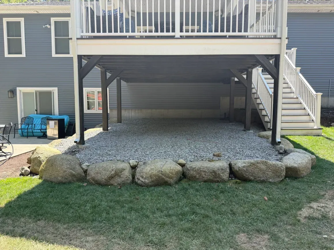 Raised deck with stairs over a gravel area bordered by large rocks and a grassy yard