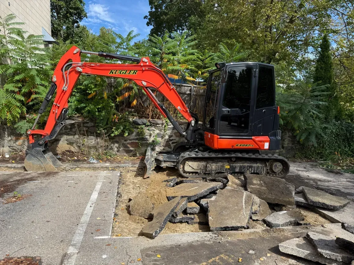 Red excavator breaking up concrete on a roadside construction site