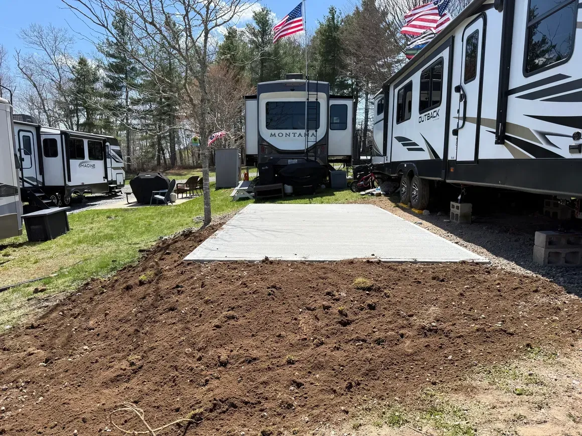 RVs parked around a concrete patio area with flags flying in a wooded campground