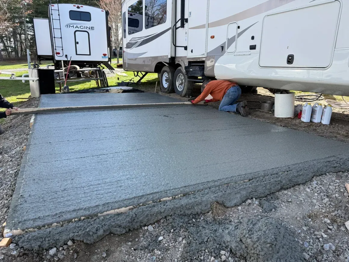Worker smoothing fresh concrete beside RVs at a campsite