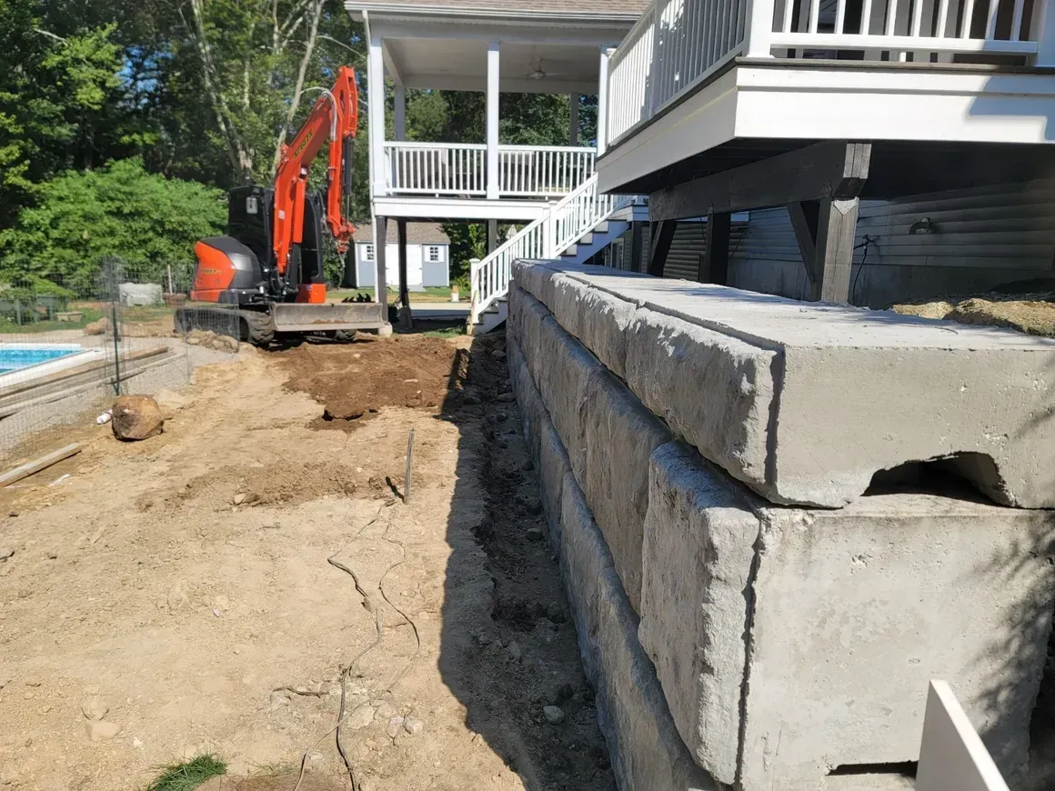 House foundation excavation beside stacked concrete blocks and an excavator at a residential site