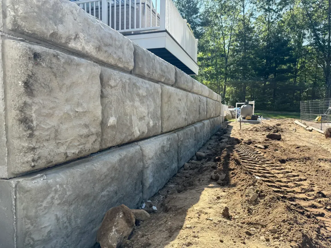 Concrete retaining wall beside a dirt construction area with stairs and trees in the background
