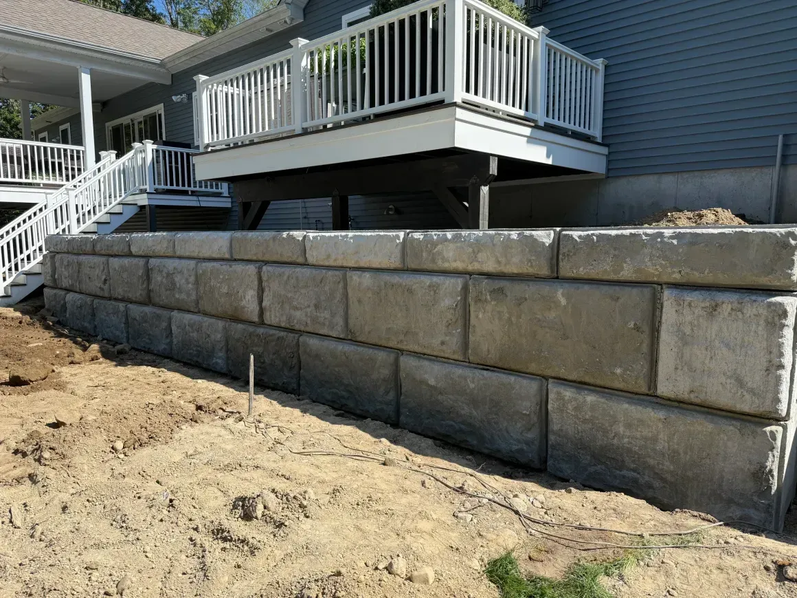 Backyard retaining wall of stacked concrete blocks beneath a raised white deck and stairs