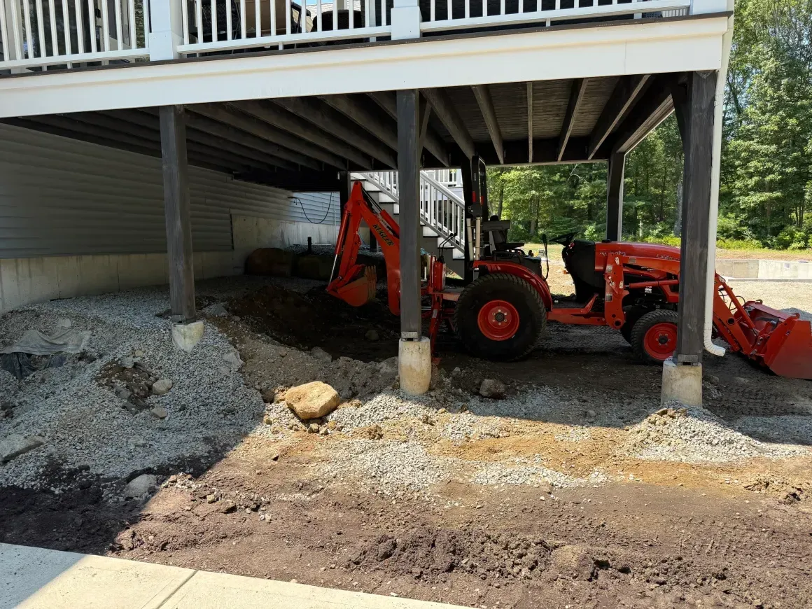 Orange tractor under a raised deck beside a gravel-covered yard