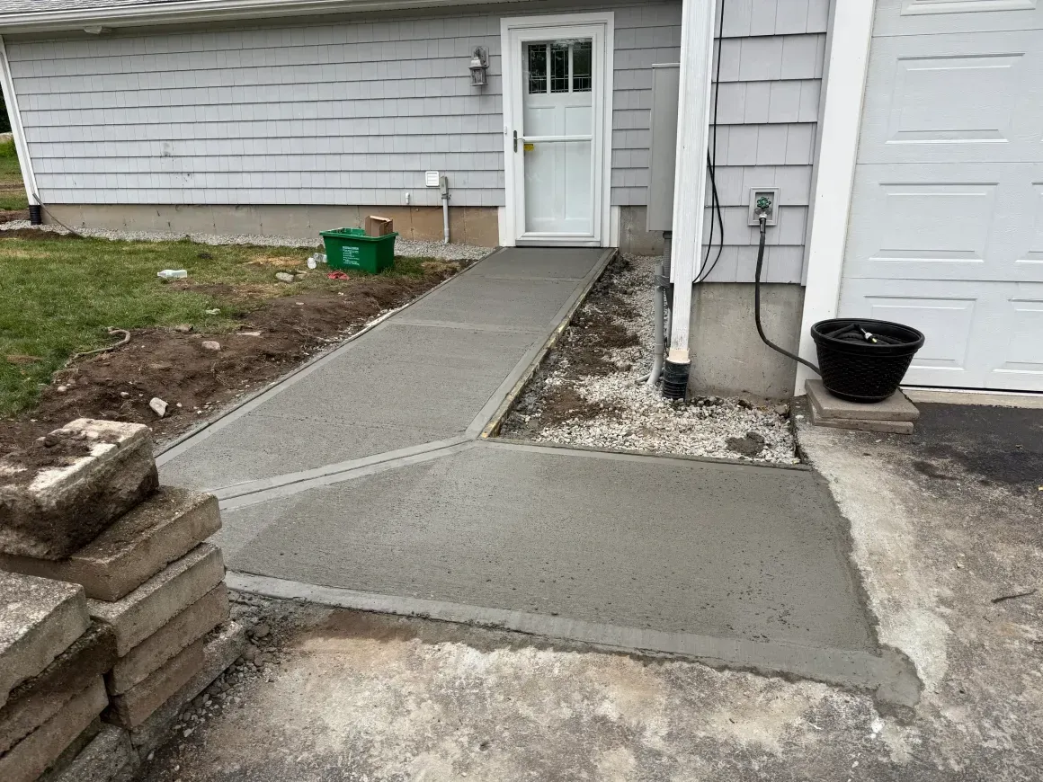 Concrete walkway leading to a back door beside a house, with fresh gray repairs and a small stoop.