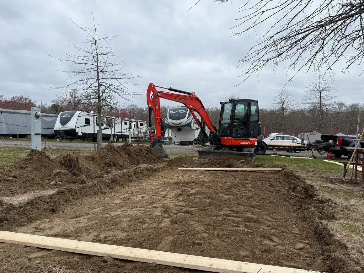 Orange excavator digging a dirt trench at a construction site under a cloudy sky